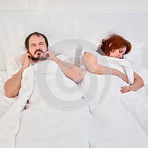 A man plugs his ears with earplugs because of the noise and snoring of his sleeping wife. Quarantine family problems due to