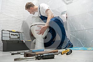 Man plumber in uniform installing toilet bowl using instrument kit professional repair service