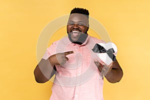 Man pointing at heart shaped gift box with excited smile, greeting on holiday and sharing present.