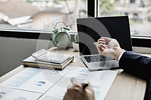 Man pointing at laptop screen and documents lying on the table, business man in black suit is sitting checking information.