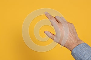 Man pointing at something against yellow background, closeup on hand. Space for text