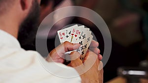 man at a poker table in a white shirt opens cards, plays poker. Cards in the hands of the player