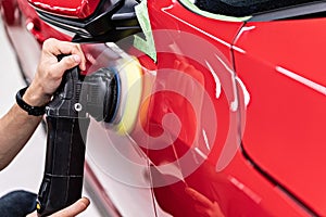 Man polishing car varnish with hand electric polisher.