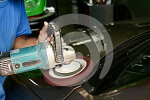 Man polishing front hood of car by burnishing machine. photo