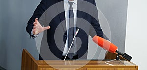 Man - politician, businessman or teacher speaks in front of microphones, leaning on podium or pulpit and gesticulating with his