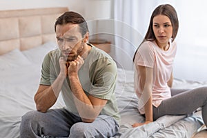 Man pondering in bed, woman sitting behind