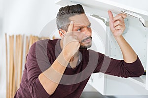 Man pondering how to repair cupboard