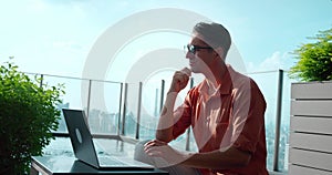 Man ponders sitting laptop near pool against cityscape. Quality, reflected thoughtful moments, symbolizes pursuit