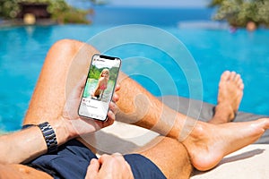 Man by the pool looking at social media app on his mobile phone