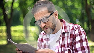 Man with poor sight trying to read newspaper in park, farsightedness, myopia