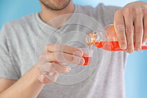 Man poring portion of liquid medicine syrup for treatment cold and flu in measuring cup. Male drinking liquid drug from