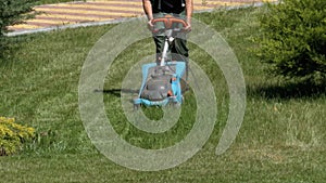Man with an Portable Electric Lawnmower Mows the Green Grass on the Lawn in the Park