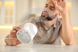 Man with portable fan suffering from heat at home, focus on hand. Summer season