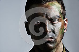 Man, portrait and camouflage with face paint for war, battle or military service on a gray studio background. Closeup of