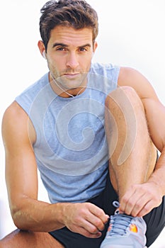 Man, portrait and tying shoes with earphones in fitness for workout or exercise against a white studio background