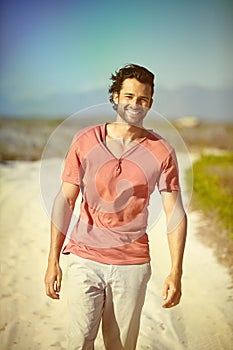 Man, portrait and walking on sand with blue sky for summer vacation, relaxation and enjoyment. Travel, sunshine and face