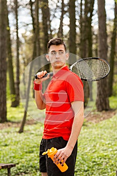 The man pose with a tennis racket and orange thermocouple, on the background of green park. Sport concept