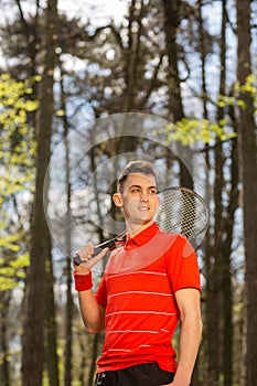 The man pose with a tennis racket and orange thermocouple, on the background of green park. Sport concept