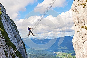 Man posing on Donnerkogel Intersport via ferrata klettersteig ladder, with his leg  hanging out, on a bright sunny day photo
