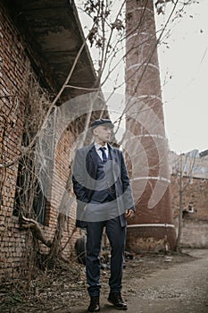 A man posing in the image of an English retro gangster dressed in Peaky blinders style near abandoned building