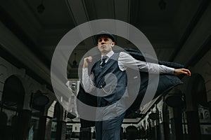 A man posing in the image of an English retro gangster in Peaky blinders style at city street