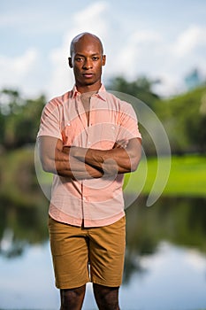 Man posing in pink button shirt with arms crossed. African American male model with deadpan expression and blurry background photo