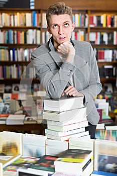 Man posing on stack of books in bookstore