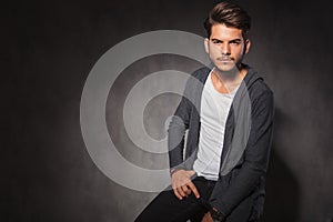 Man posing in studio with hand in pocket while sitting