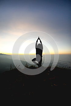 Man posing yoga on top of misty mountain cliff