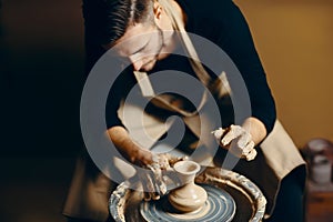 Man potter working on potters wheel making ceramic pot from clay in pottery workshop