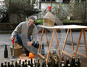 Man pour red wine from the demijohn to glass bottles