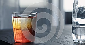 man pour syrup into tonic water with clear ice ball in tumbler glass on black oak table