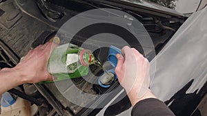 The man is pouring antifreeze liquid in a car