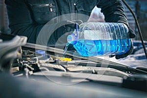 Man pouring an antifreeze liquid in a windshield washer tank of a car