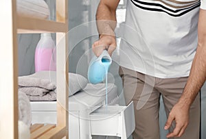 Man pouring detergent into washing machine drawer in bathroom. Laundry day