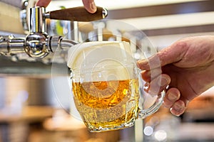 A man pouring draft lager beer into a dimpled glass mug  in a modern pub. Overflowing glass