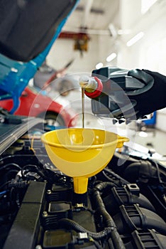 Man pouring engine oil into car motor through funnel