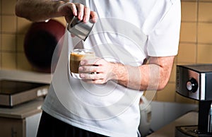 Man pouring frothed milk into espresso for making a latte