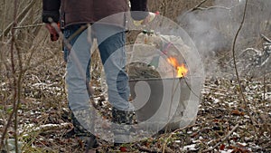 Man is pouring fuel over plastic garbage. A homeless man burns trash in an iron barrel. Environmental pollution