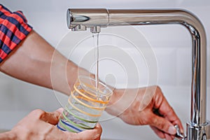 Man pouring glass of water from tap with clean filter in kitchen, close up