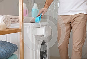 Man pouring laundry detergent into washing machine drawer in bathroom