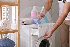 Man pouring laundry detergent into washing machine drawer in bathroom