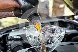 A man is pouring machine oil into a car engine through a homemade funnel. Changing the machine oil