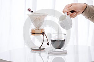 Man pouring milk into glass with cold brew coffee on table