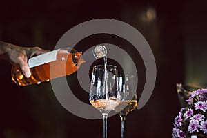 Man pouring rose wine from bottle into glass indoors.