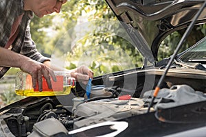 Man pouring some windshield washer fluid in the special compartment under the hood of the car. Filling liquid reservoir tank with