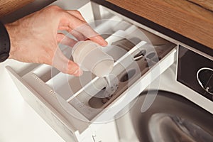 Man pouring the washing fabric conditioner into the washing machine to get more softer clothes