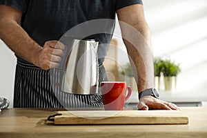 Man pouring water into mug. Kitchen table background with kitchen tools. Space for your decoration or advertising product.