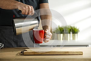 Man pouring water into mug. Kitchen table background with kitchen tools. Space for your decoration or advertising product.