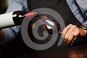 Man pouring wine into wineglass, male hand holding bottle
